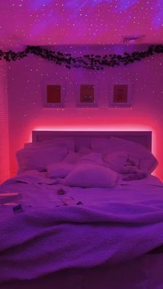 a bed in a room with purple lights on the ceiling and white linens all over it