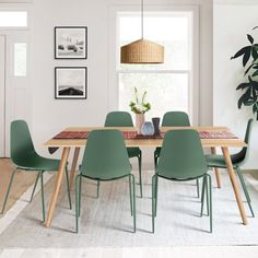 a dining room table with green chairs in front of a window and potted plant