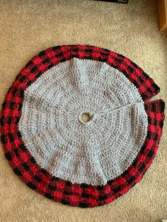 a crocheted red and black round rug on the floor next to a remote control