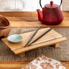 chopsticks, teapot and bowl sitting on a wooden table with place mats