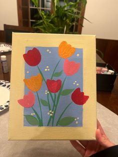 a hand holding up a small card with flowers on it and hearts painted on the front