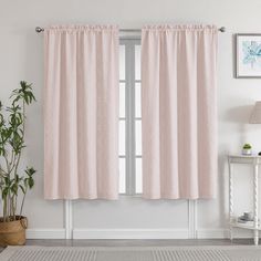 a living room with pink curtains and a white rug in front of the window, next to a potted plant