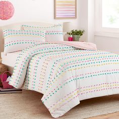 a bed with white sheets and colorful polka dot design on the comforter, next to a potted plant