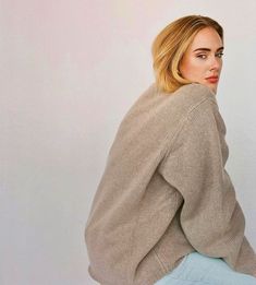 a woman with blonde hair wearing a beige sweater and light blue jeans is looking off to the side