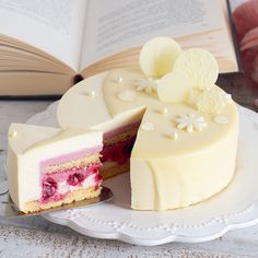 a piece of cake on a plate next to an open book and some pink flowers