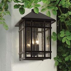 an outdoor light hanging on the side of a building next to a tree with green leaves