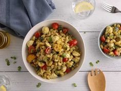 a white bowl filled with pasta salad next to two wooden spoons and glassware