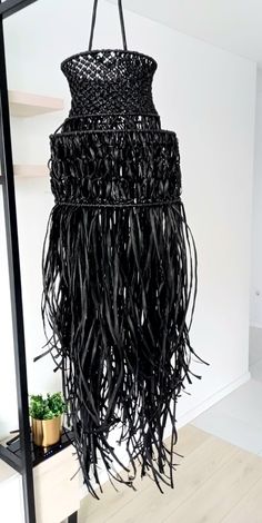 a large black hanging object with fringes on it's sides and a plant in the background