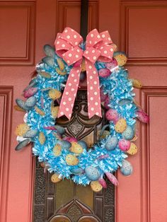 a pink and blue wreath with polka dot bows on the front door to a house