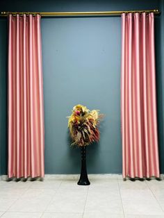 a vase with some flowers in it next to two pink drapes on a blue wall