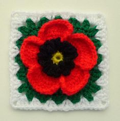 a crocheted square with a red flower on the center and green leaves in the middle