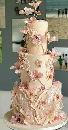 a three tiered wedding cake with pink flowers on the top and bottom, sitting on a white table