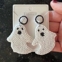 a pair of white and black beaded ghost earrings on top of a card board