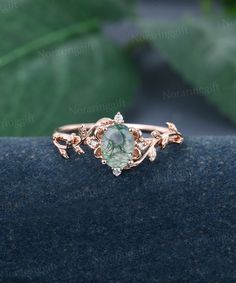 a ring with an oval green stone surrounded by small white and rose gold leaves on it