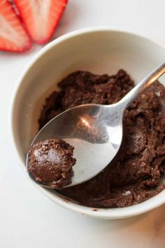 a white bowl filled with chocolate pudding and a spoon next to strawberries on a table