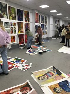 people looking at art work on the floor in an office space with posters all over the floor