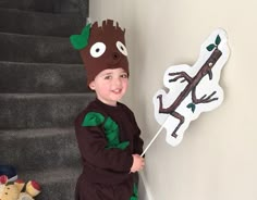 a little boy dressed up as a tree with leaves on his head and holding a stick