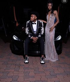 a man and woman sitting on top of a car in front of a dark background