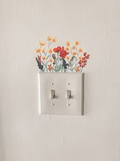 an electrical outlet with flowers painted on the wall and two light switch plates attached to it