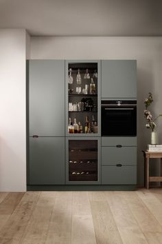 a kitchen with grey cabinets and wooden flooring is shown in this image, there are bottles on the shelves