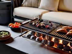 an outdoor grill with food on it and bowls of salads next to the grill