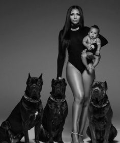 a woman in a bodysuit standing next to three dogs and holding a baby on her lap