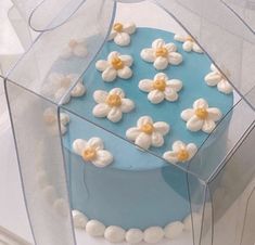 a blue cake with white and yellow flowers on it sitting in a clear plastic box