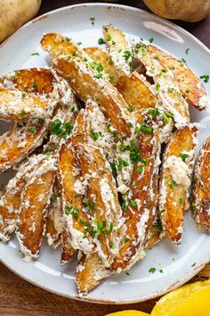 fried potatoes with parmesan cheese and chives on a white plate next to lemons