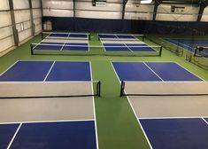 two tennis courts with blue and green flooring in an indoor gym area that is empty