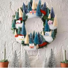 a christmas wreath hanging on the wall next to potted plants and small pine trees