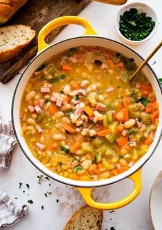 a yellow pot filled with soup next to bread and other food on a white table