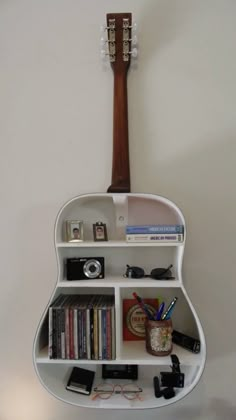 a guitar shaped shelf with books, cd's and other items on it against a white wall