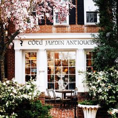 an outside view of a building with flowers on the ground and tables in front of it