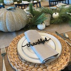 a place setting for thanksgiving dinner with silverware and napkins, pine branches in the background