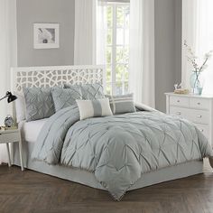 a bed with grey comforter and pillows in a room