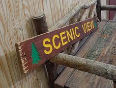 a wooden bench sitting next to a wooden fence with writing on it and pine trees painted on the back