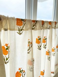 an orange flowered curtain hanging in front of a window with white curtains and windowsills