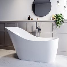 a large white bath tub sitting next to a sink in a bathroom under a round mirror