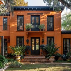 an orange house with potted plants in front of it and stairs leading up to the second floor