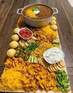 a platter filled with chips and dips on top of a wooden table next to a pot of soup