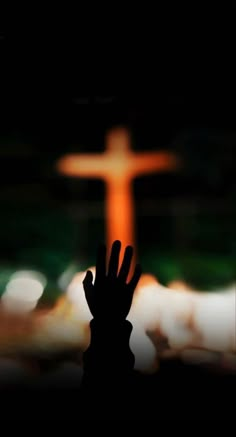 the silhouette of a person's hand in front of a blurry image of a cross