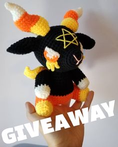 a hand holding a small crocheted toy with an orange and black outfit on it