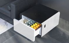 an open drawer on the side of a table with drinks and fruit in it next to a couch