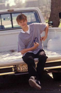 a young man sitting on the hood of a car with his hands in his pockets