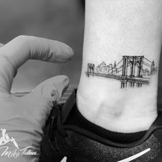 a tattoo on the ankle of a person with a city skyline in the back ground