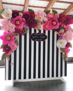 a black and white striped wall with flowers on the side, along with pink and red flowers