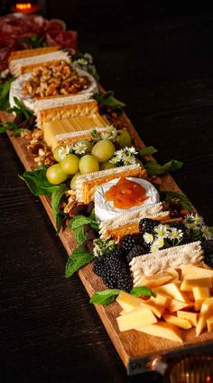 an assortment of cheeses, crackers and fruit on a wooden platter with leaves