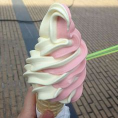 a hand holding an ice cream cone with pink and white icing