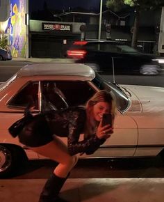 a woman leaning against a car while looking at her cell phone