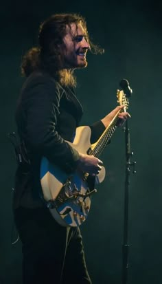 a man with long hair holding a guitar and singing into a microphone at a concert